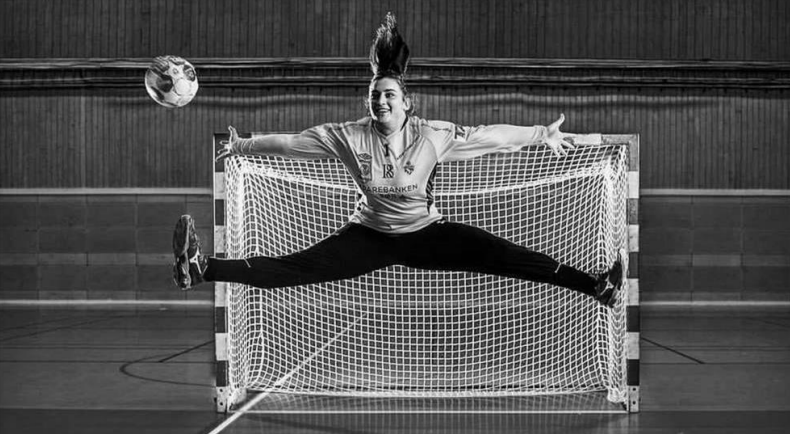 Handball-Torwartin springt mit gespreizten Beinen im Tor, Ball in der Luft.